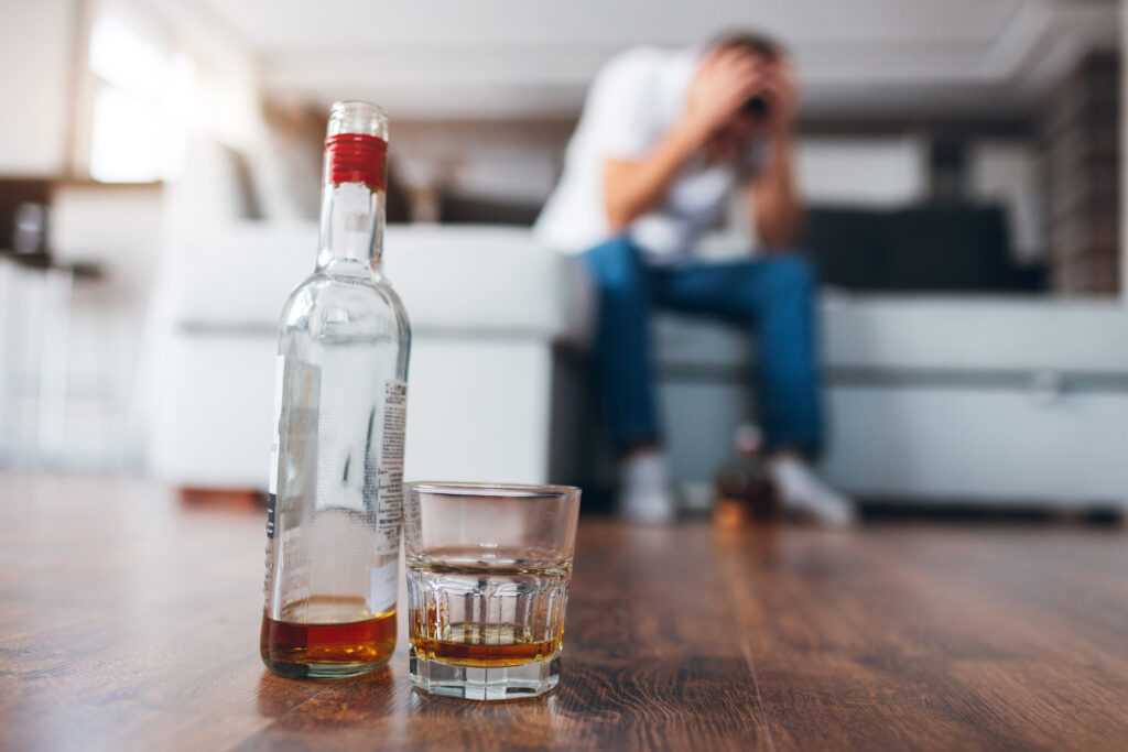 Mężczyzna siedzi na kanapie, trzymając się za głowę i chcąc powstrzymać ochotę na napicie się alkoholu.